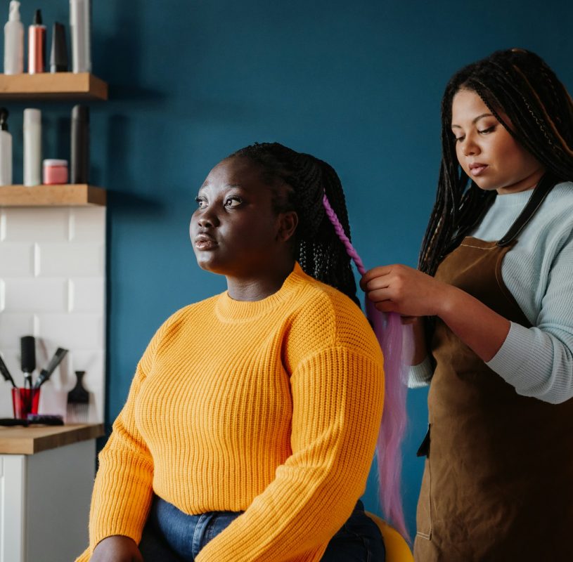 Confident African American hairdresser braiding hair to a female customer in salon